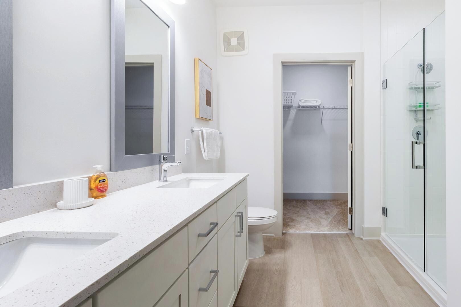 A modern bathroom with a large mirror, two sinks, a toilet, and a glass shower enclosure.