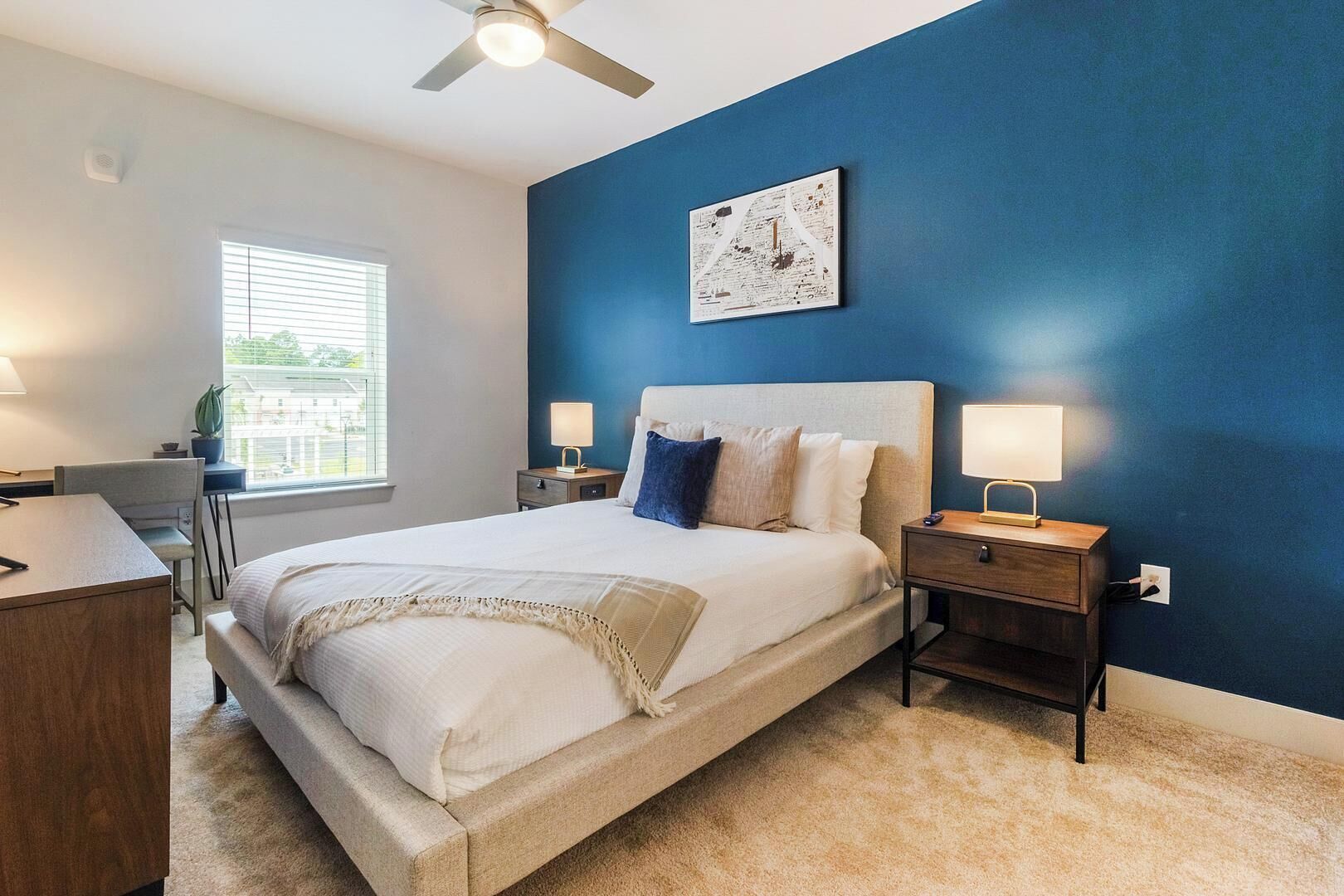 A bedroom with a bed, bedside tables, a desk, and a window.