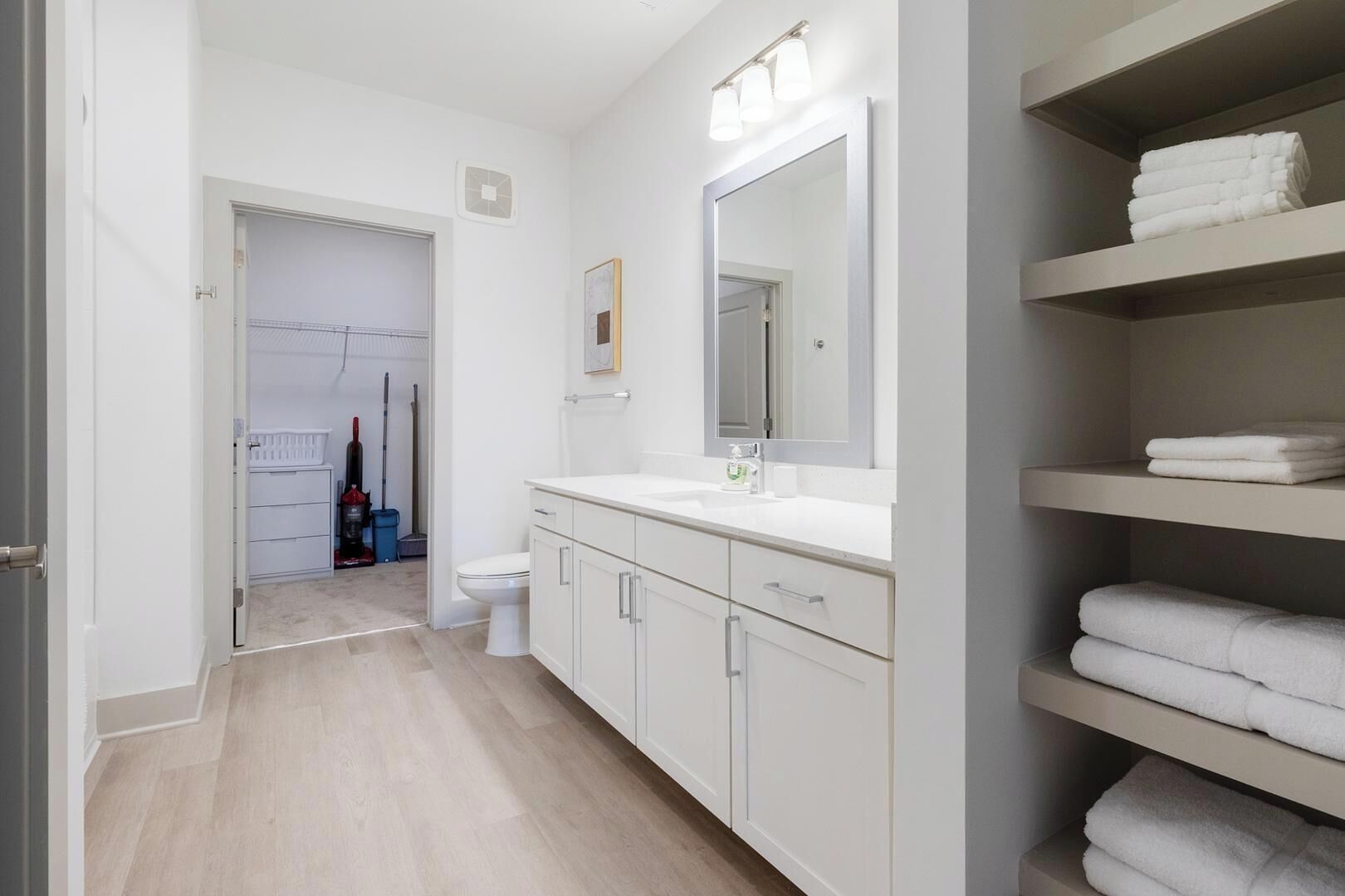 A modern bathroom with a white sink, mirror, and shelves for towels.