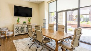 A conference room with a large table, six chairs, a television on the wall, and a view of the outdoors through large windows.