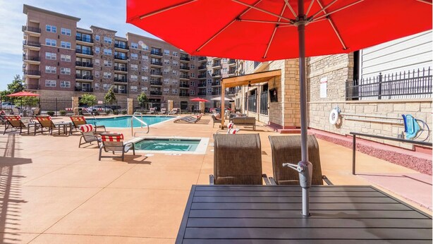 A pool area with lounge chairs and umbrellas, surrounded by multi-story buildings.