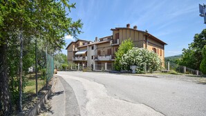Un immeuble de deux étages doté de balcons, une route pavée devant et une clôture sur le côté gauche.