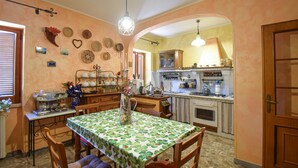 Une cuisine chaleureuse avec un coin repas, comprenant une table recouverte d’une nappe à motifs floraux, des chaises en bois et un luminaire suspendu.