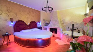 Une chambre à coucher avec un lit rond, une cheminée en pierre, un lavabo et un lustre.