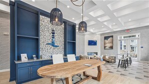 A modern hotel lobby with a large wooden table, blue cabinets, and a mosaic wall. - Landing | Stylish 2BD, Pool, Gym (Leland)