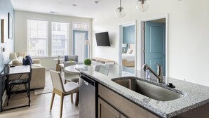 A modern kitchen with a granite countertop, stainless steel sink, and pendant lighting. - Landing | Spectacular 2BD, Pool, Gym (Leland)