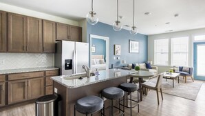 A modern kitchen with a central island, bar stools, and a dining area with a table and chairs. - Landing | Spectacular 2BD, Pool, Gym (Leland)