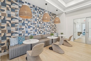 Un área de descanso moderna con un muro de diseño geométrico, un sofá gris, sillones de mimbre y mesas redondas.