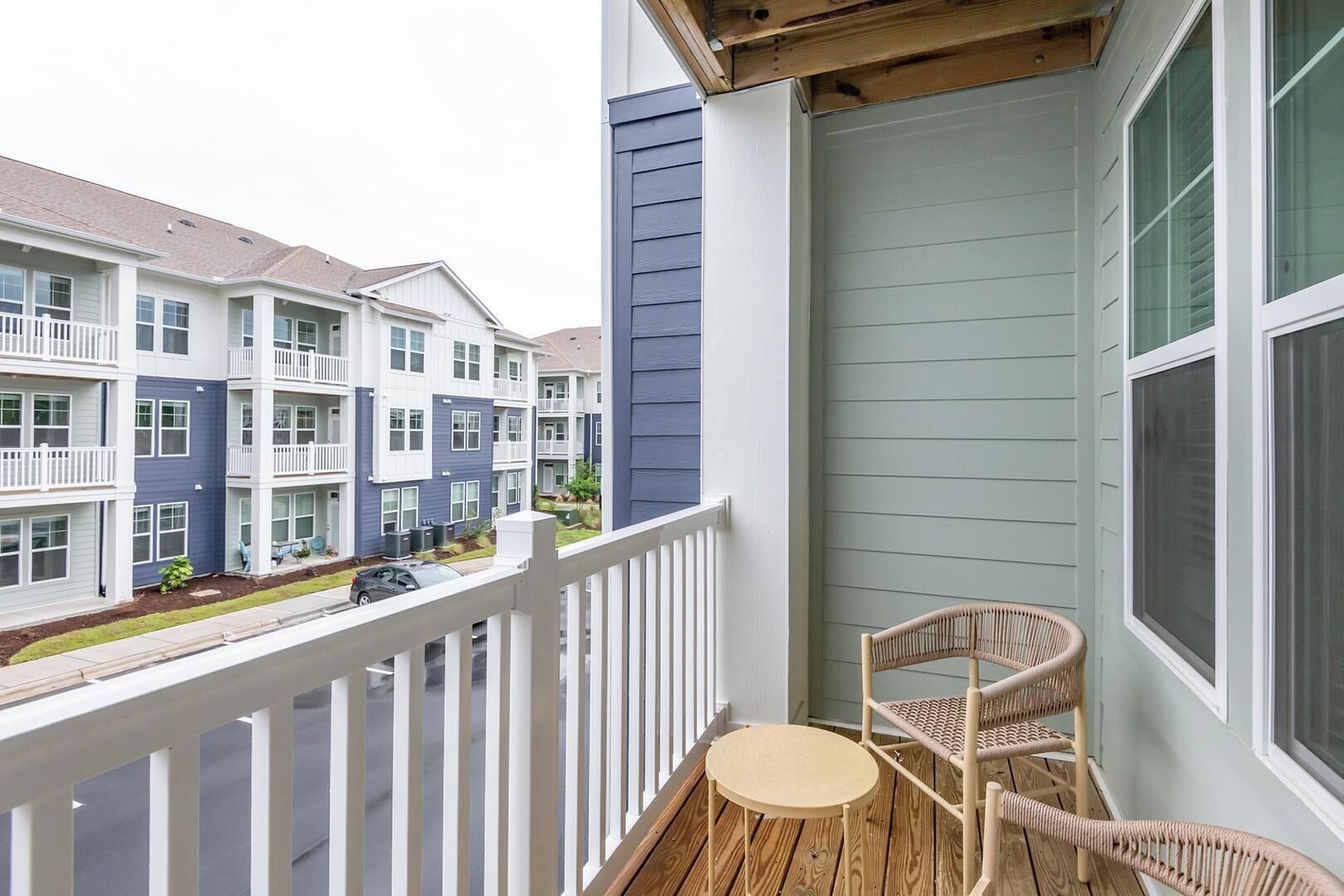 A balcony with a wooden floor, two wicker chairs, and a small round table.