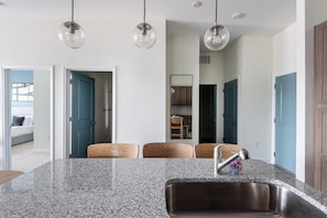Cozinha moderna com bancadas de granito, pia de aço inoxidável e cadeiras de madeira.