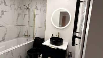 Une salle de bain avec une baignoire, un grand miroir rond avec éclairage intégré, un lavabo noir et un meuble-lavabo noir.