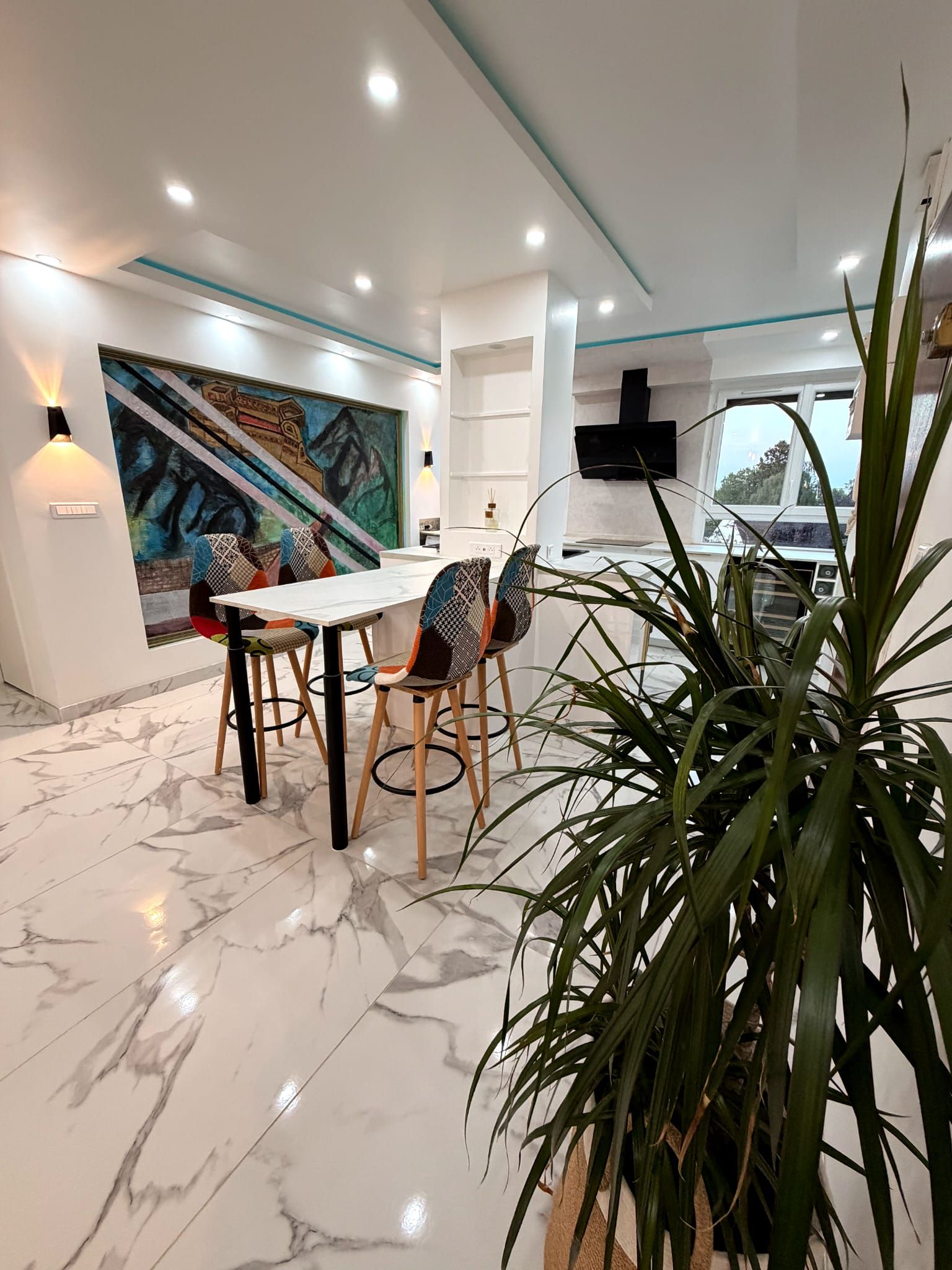 Un comedor moderno con piso de mármol, una mesa con sillas, un cuadro grande en la pared y una planta en maceta.