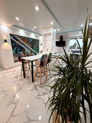 Un espace repas moderne avec un sol en marbre, une table entourée de chaises, un grand tableau accroché au mur et une plante en pot.