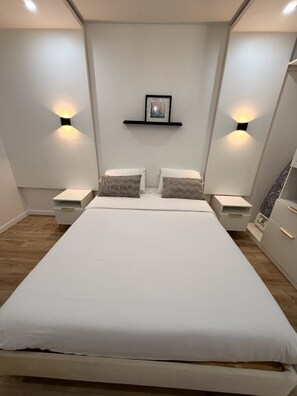 Une chambre moderne avec un grand lit, deux tables de chevet et des lampes fixées au mur.