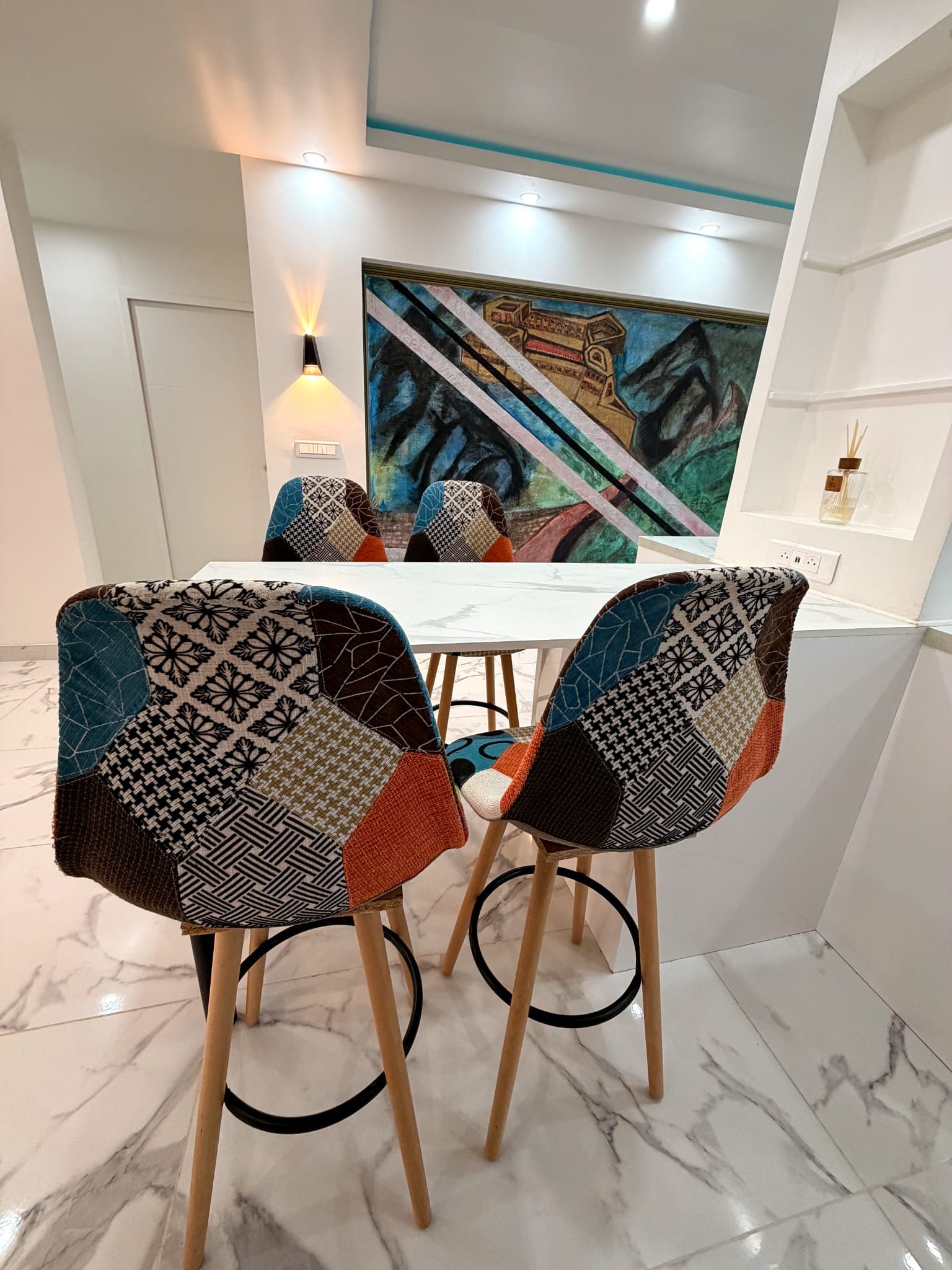 Un área de comedor con dos sillas tapizadas en tela estampada, una mesa blanca y un cuadro en la pared.