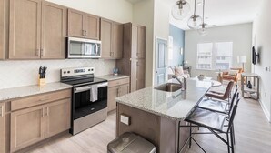 A modern kitchen with wooden cabinets, a stainless steel oven, and a large island with a sink. - Landing | Beautiful 1BD, Clubhouse, Pool (Leland)