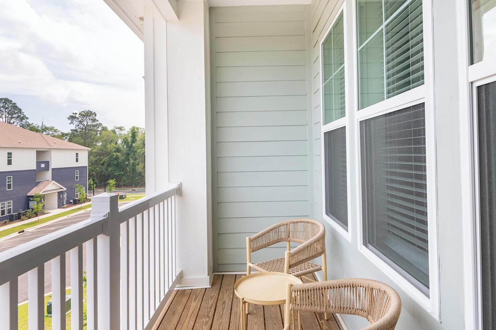 A balcony with a white railing, two wicker chairs, and a small round table.