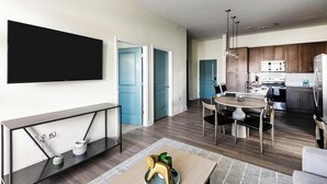 Una sala moderna con un televisor de pantalla plana, una mesa consola y un comedor con una mesa redonda y sillas.