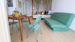 A compact living space with a dining table, teal chairs, a green sofa, and a TV on a white cabinet. - La Terrasse du Gosier (Le Gosier)