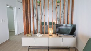 A modern living room with a TV on a white cabinet, a woven lamp, and a wooden partition with hanging plants. - La Terrasse du Gosier (Le Gosier)