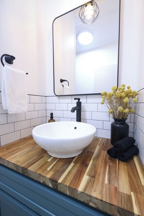 Ein Badezimmer mit einem weißen Waschbecken, einer Holz-Arbeitsplatte, einem schwarzen Wasserhahn und einem Spiegel mit Beleuchtung.