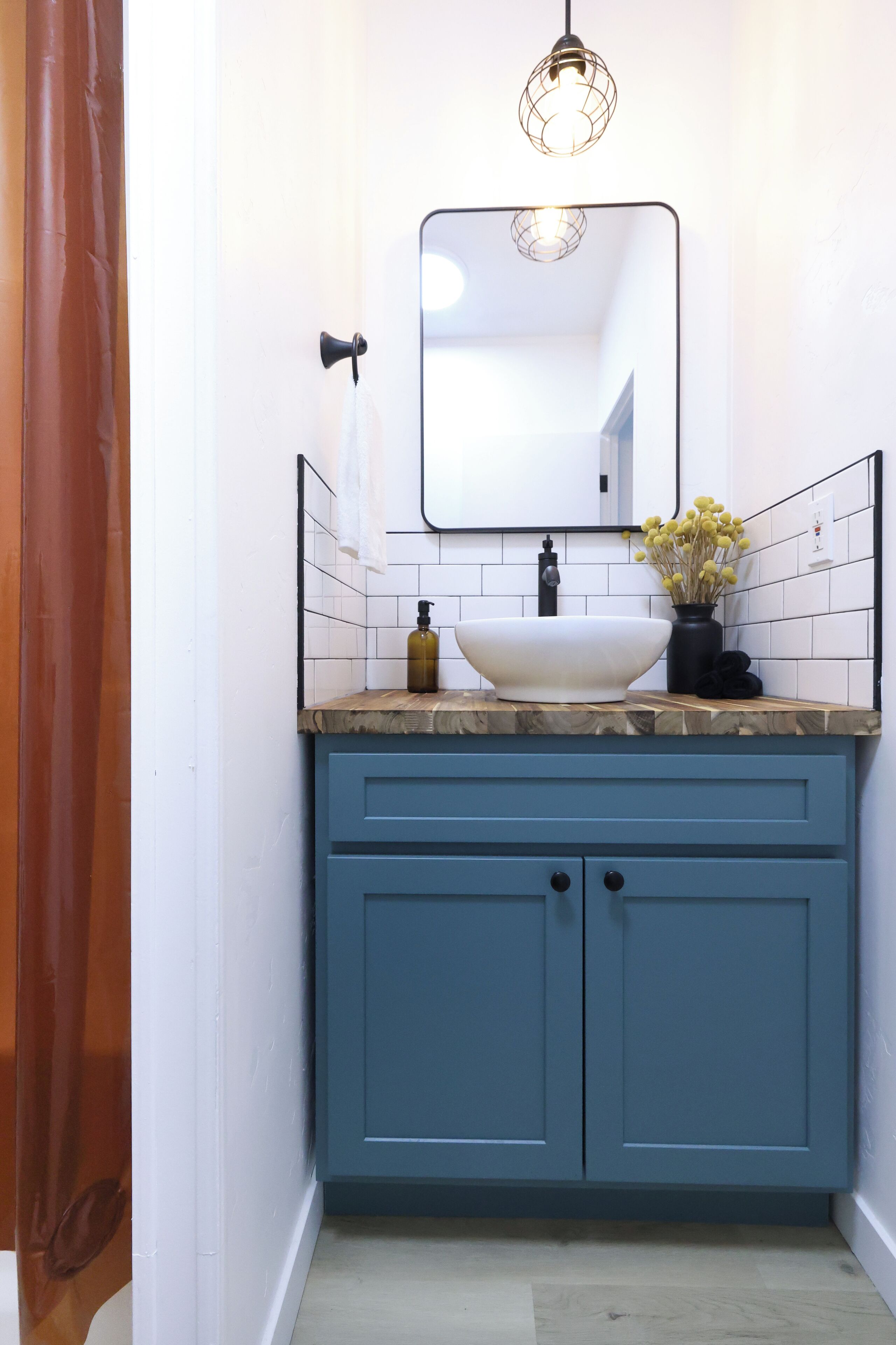 A bathroom with a white sink, blue cabinets, a mirror, and a hanging light fixture.