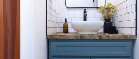 A bathroom with a white sink, blue cabinets, a mirror, and a hanging light fixture.