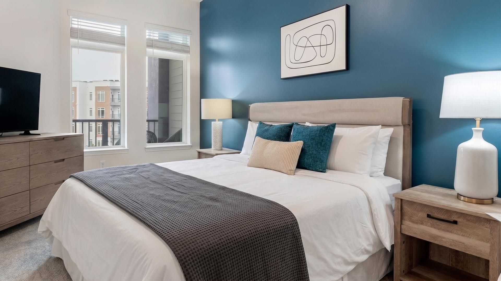 A hotel room with a bed, bedside tables, a TV, and a view of the outside.
