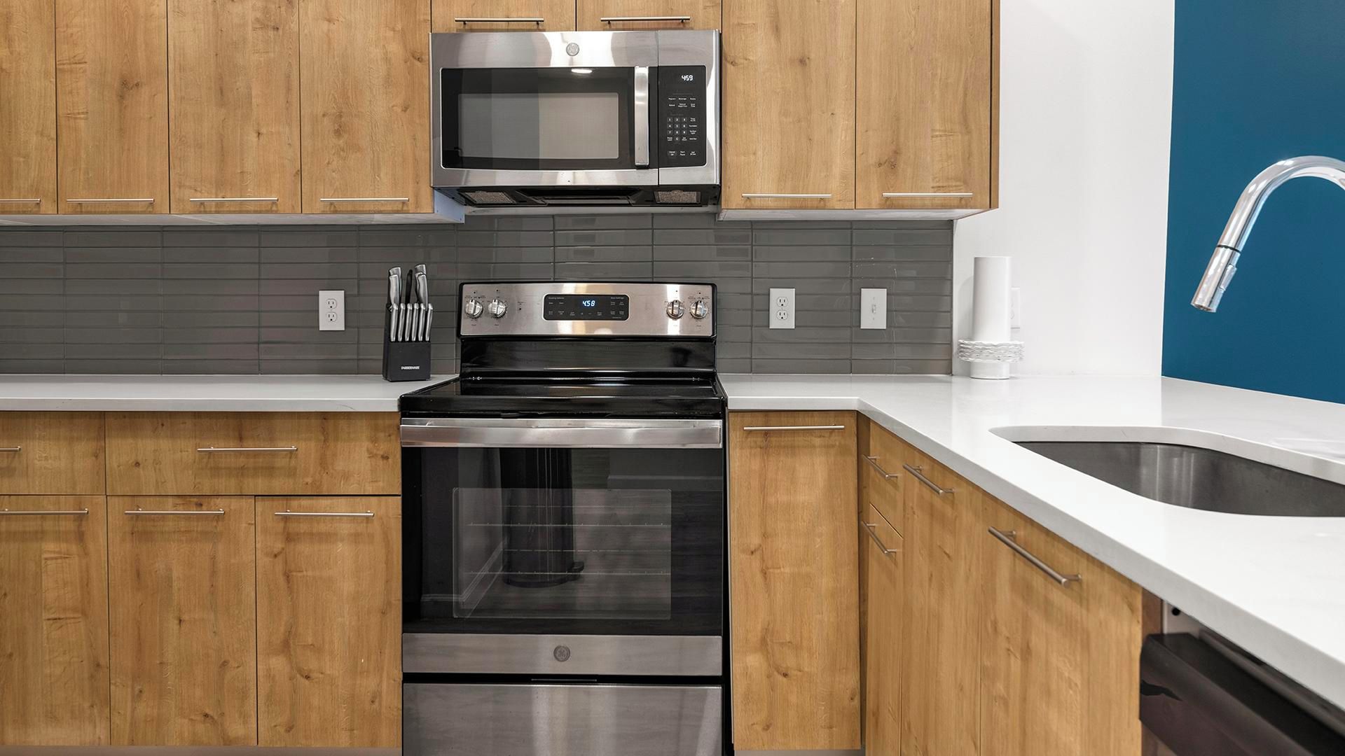 Eine Küche mit Holzschränken, einer Edelstahl-Mikrowelle, einem Backofen und einem Waschbecken mit modernem Wasserhahn.