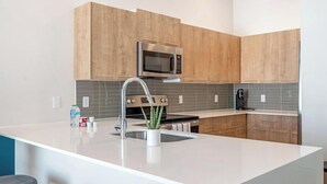 A modern kitchen with wooden cabinets, a stainless steel microwave, a sink with a faucet, and a countertop with a plant.