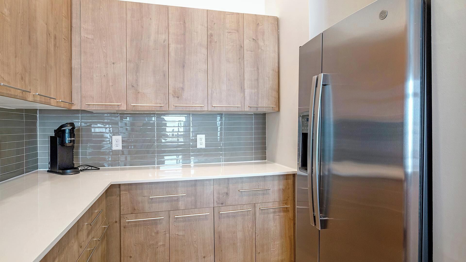 A modern kitchen with wooden cabinets, a stainless steel refrigerator, and a coffee maker.