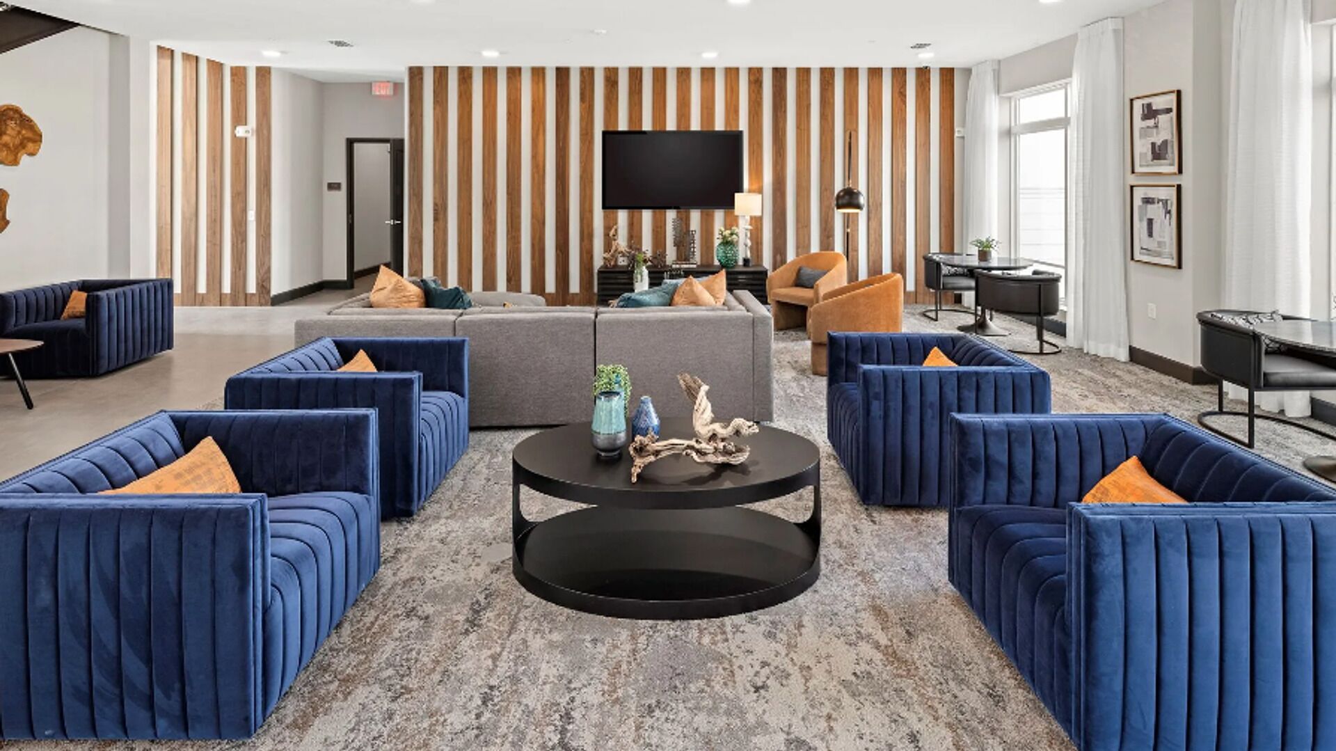 Een moderne woonkamer met blauwe banken, een centrale salontafel en een flatscreen televisie aan de muur.