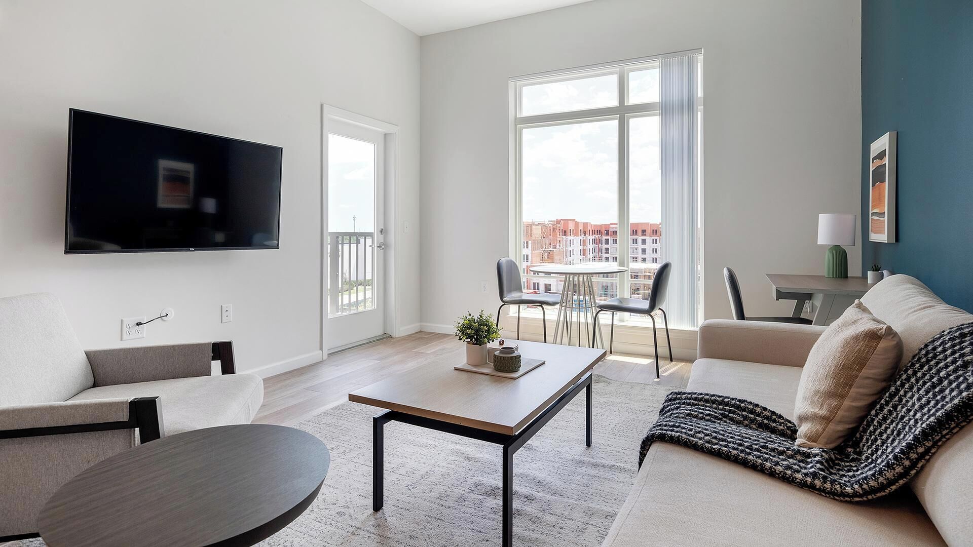 A modern living room with a flat-screen TV, a sofa, a coffee table, and a dining area with chairs and a table.