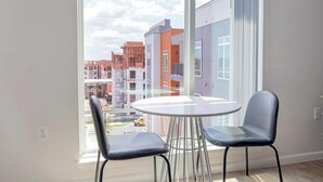 A room with a large window, two chairs, a small round table, and a view of a cityscape with buildings and construction.