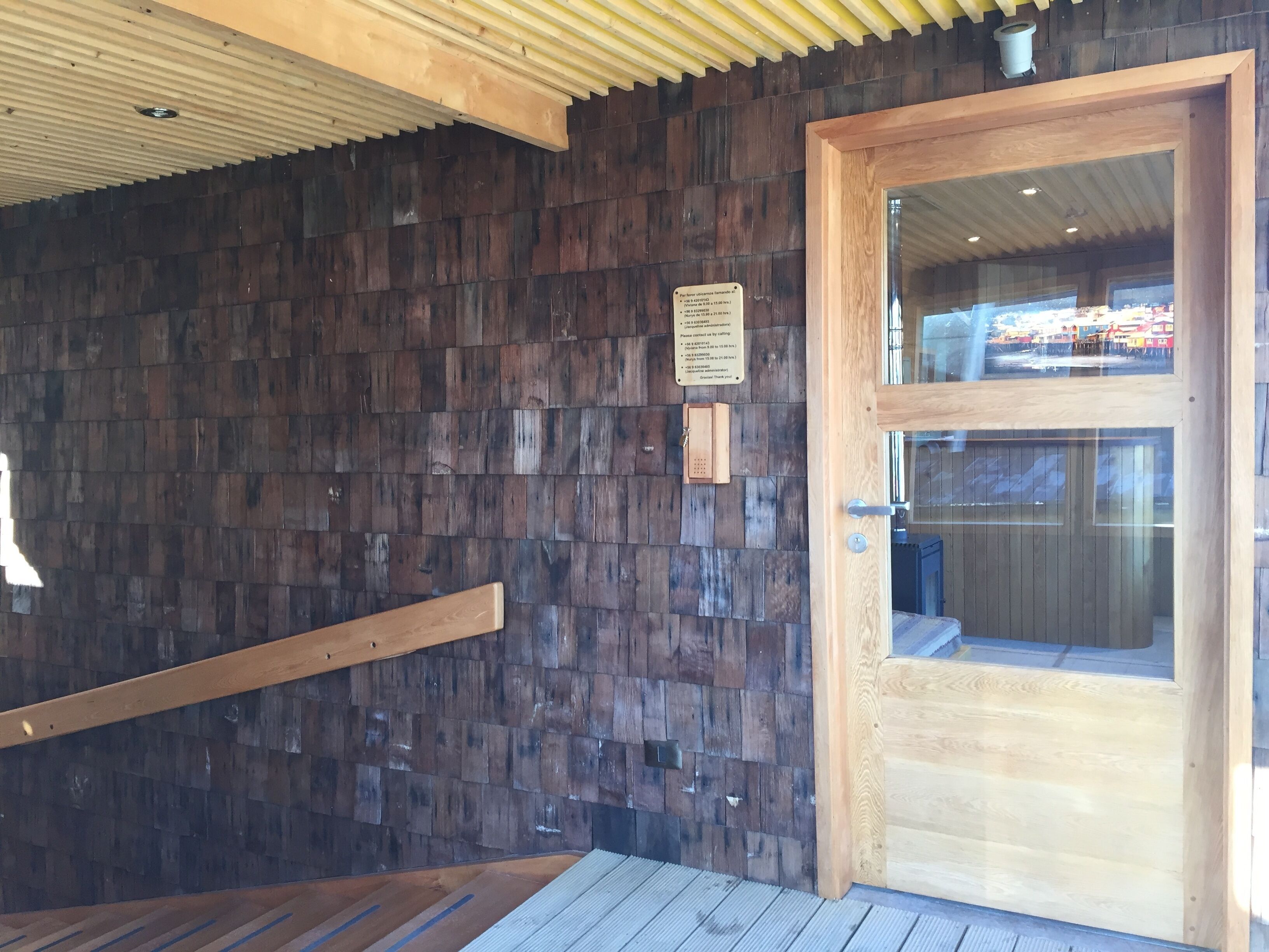 A wooden door with a glass panel, a wooden wall with a textured pattern, and a metal handrail.