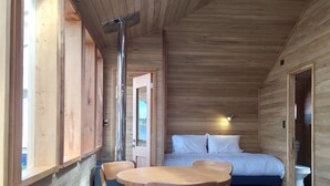 A wooden cabin with a bed, a table with chairs, and a window. - Palafito Azul Apart Hotel (Castro)