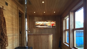 A wooden cabin interior with a central fireplace, a wooden bench, and a window with a view of houses. - Palafito Azul Apart Hotel (Castro)