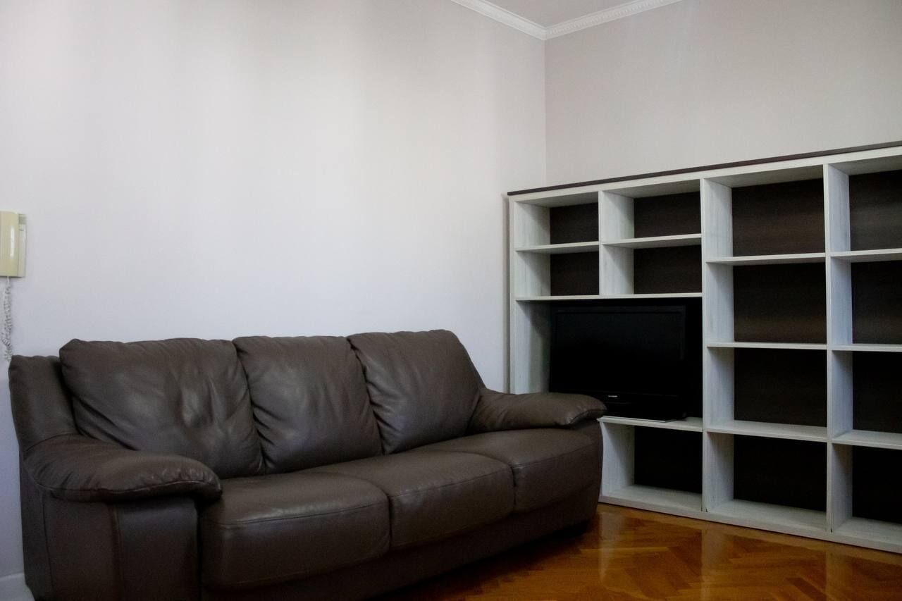 Ein Wohnzimmer mit einem braunen Ledersofa, einem weißen Regal und einem Holzboden.