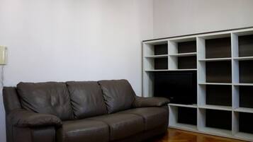 Ein Wohnzimmer mit einem braunen Ledersofa, einem weißen Regal und einem Holzboden.