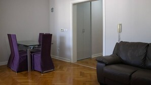 Una habitación con una mesa de vidrio, dos sillas moradas, un sofá de cuero marrón y un armario.