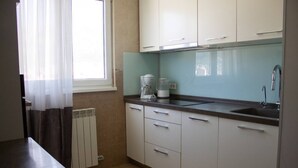 Una cocina con gabinetes blancos, una encimera, una cafetera y un ventanal con cortinas.