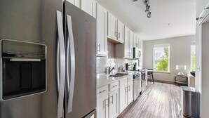Una cocina moderna con electrodomésticos de acero inoxidable, armarios blancos y un amplio ventanal que proporciona luz natural.