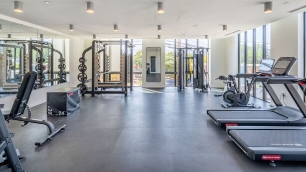 A modern gym with various exercise equipment, large windows, and a clean, spacious layout.