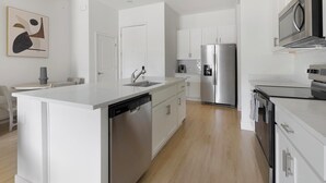A modern kitchen with white cabinetry, stainless steel appliances, and a central island with a dishwasher. - Landing | Incredible 2BD, Pool (Casas Adobes)