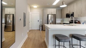 A modern kitchen with stainless steel appliances, a white island with bar stools, and wooden cabinetry.