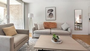 A modern living room with a grey sofa, a beige armchair, a coffee table with a plant, a floor lamp, and a framed artwork on the wall.