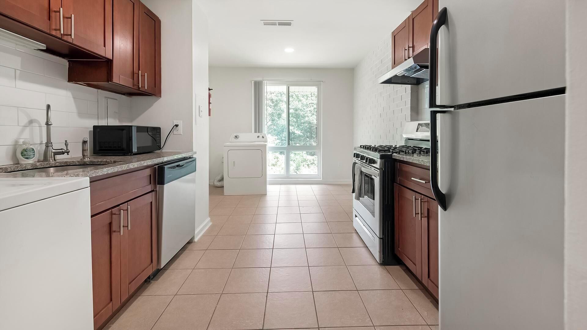 A modern kitchen with wooden cabinets, a dishwasher, a microwave, a stove, and a refrigerator.