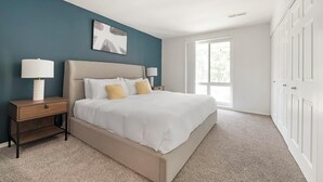 A bedroom with a bed, nightstands, a lamp, a painting, and a large window.