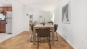 A modern kitchen with white cabinets, a white refrigerator, and a dining area with a wooden table and four chairs.
