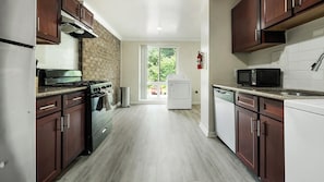 A kitchen with a brick wall, stainless steel appliances, and a view to the outside. - Landing | Spectacular 1BD, Gym, Pool (Greenbelt)